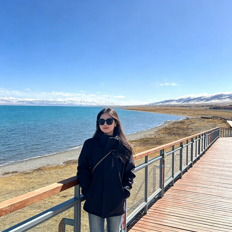 Female tourist posing on the viewing platform by Qinghai Lake with distant mountain backdrop