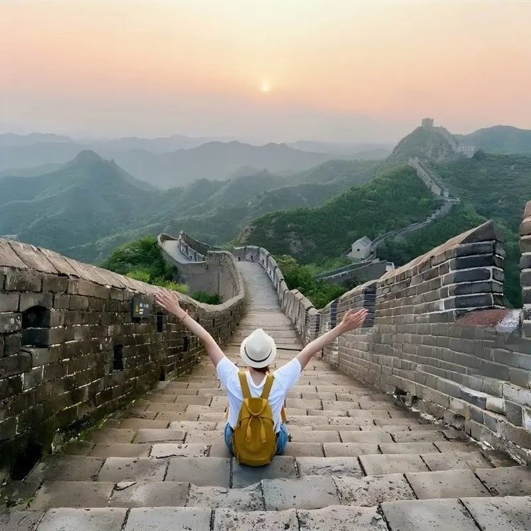 Female traveler sitting on the Great Wall steps with arms outstretched at sunrise, Jinshanling Great Wall near Beijing