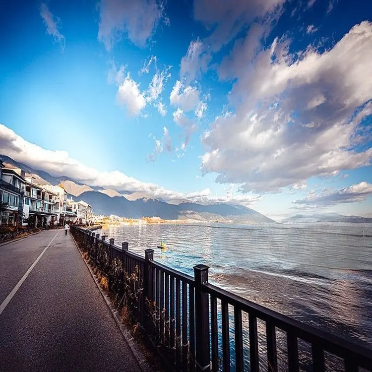 Dali Erhai Lake ecological corridor lakeside path with Bai architecture, calm water and Cangshan Mountain backdrop under blue sky, Yunnan China
