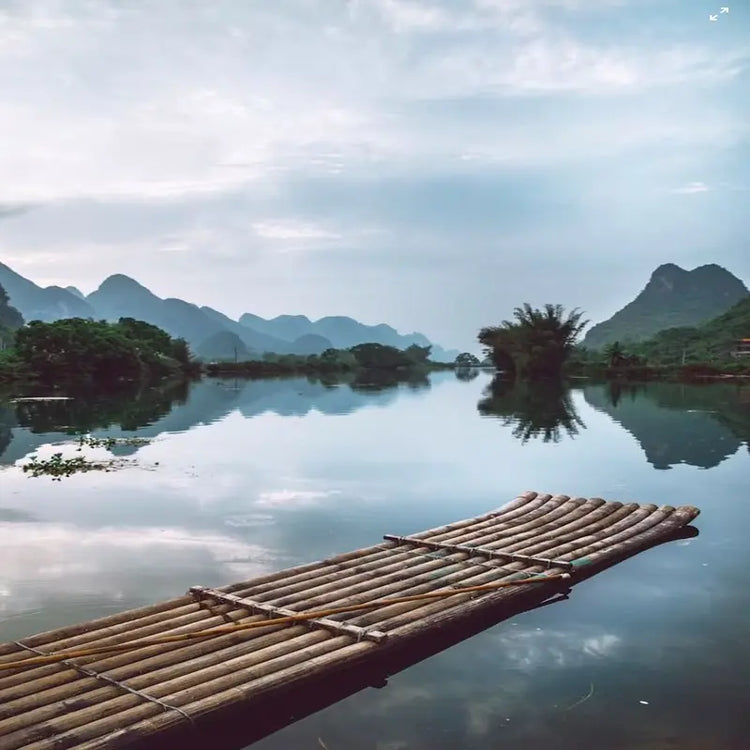 Empty bamboo raft on calm Yulong River with perfect reflection of karst mountains, Yangshuo Guilin Guangxi China, peaceful morning mist