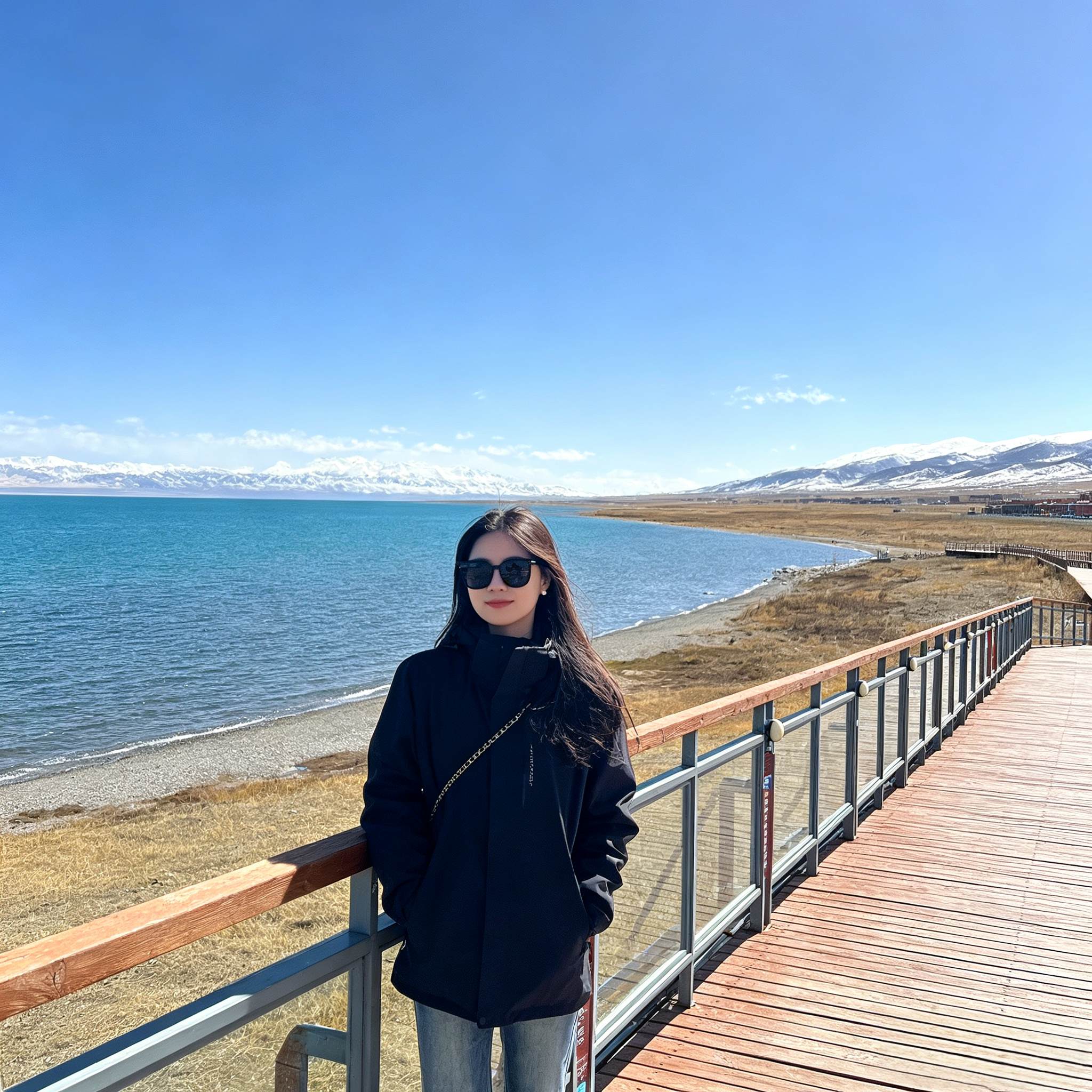 Female tourist posing on the viewing platform by Qinghai Lake with distant mountain backdrop