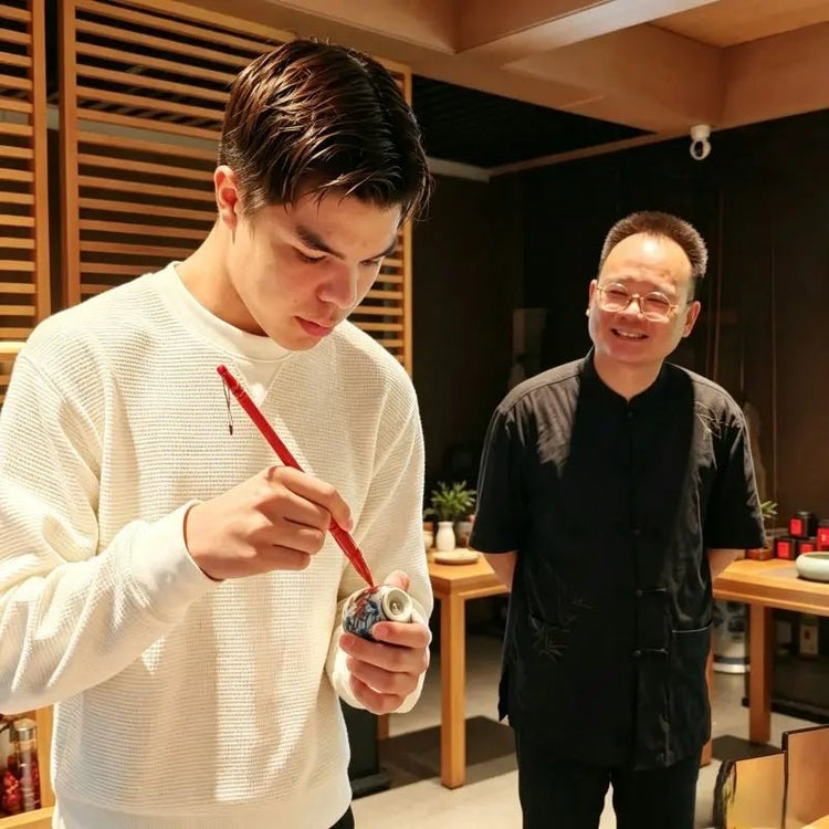 Young guest hand-painting a zodiac Ru porcelain teacup during Chinese tea culture experience