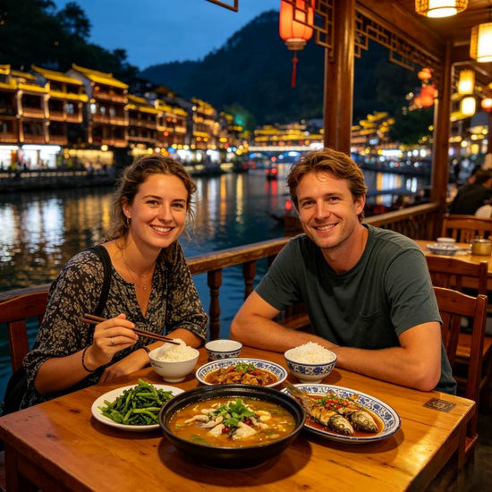 Western couple enjoying local sour soup fish dinner by riverside, Fenghuang Ancient Town, Hunan Province, China