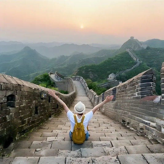 Female traveler sitting on the Great Wall steps with arms outstretched at sunrise, Jinshanling Great Wall near Beijing