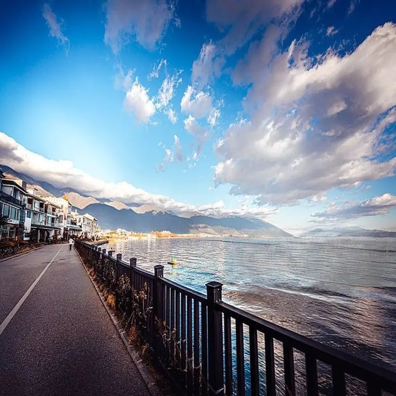 Dali Erhai Lake ecological corridor lakeside path with Bai architecture, calm water and Cangshan Mountain backdrop under blue sky, Yunnan China
