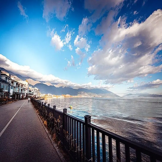 Dali Erhai Lake ecological corridor lakeside path with Bai architecture, calm water and Cangshan Mountain backdrop under blue sky, Yunnan China